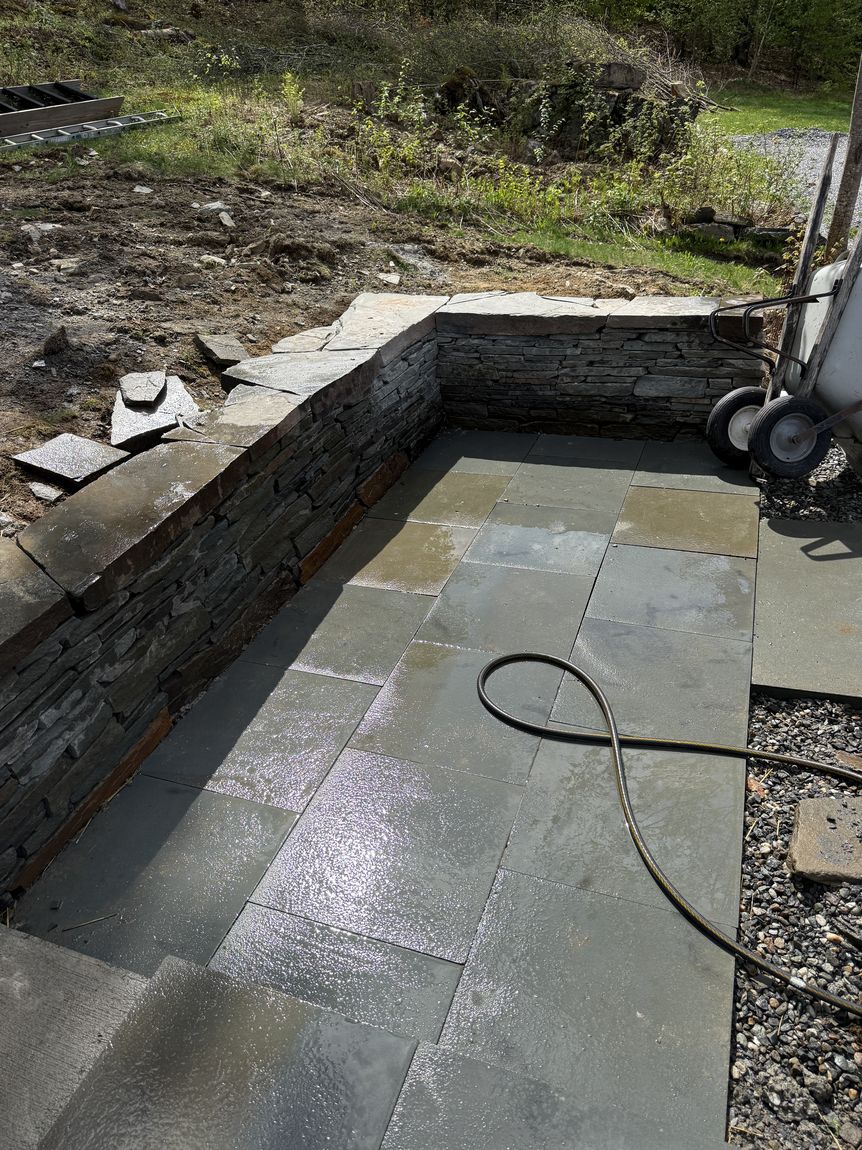Stacked stone retaining wall beside a fresh bluestone patio